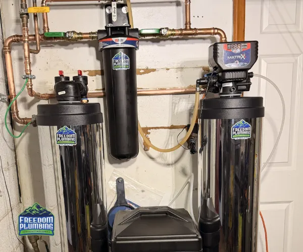 Close-up of a corroded copper pipe joint with heavy white mineral deposits and green oxidation in a dark utility area.